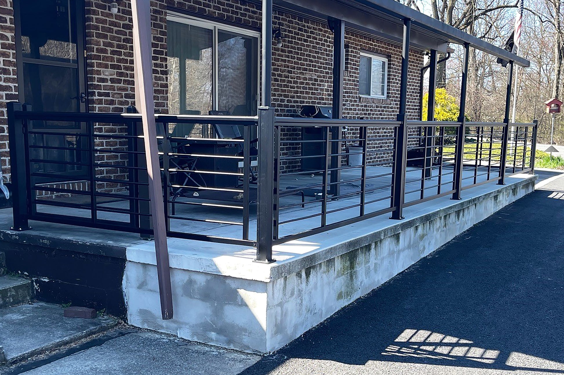 Outdoor patio area with a brick building, table, chairs, and Weatherables Georgetown black aluminum rod railing.