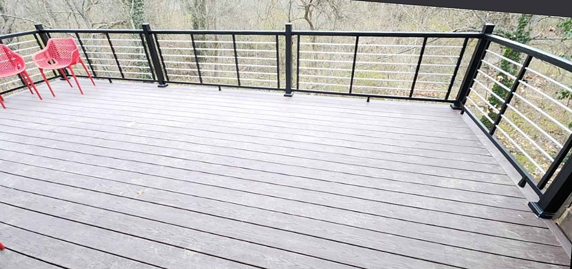Wooden deck with Weatherables Cornell black and silver aluminum rod railing and red chairs in the background