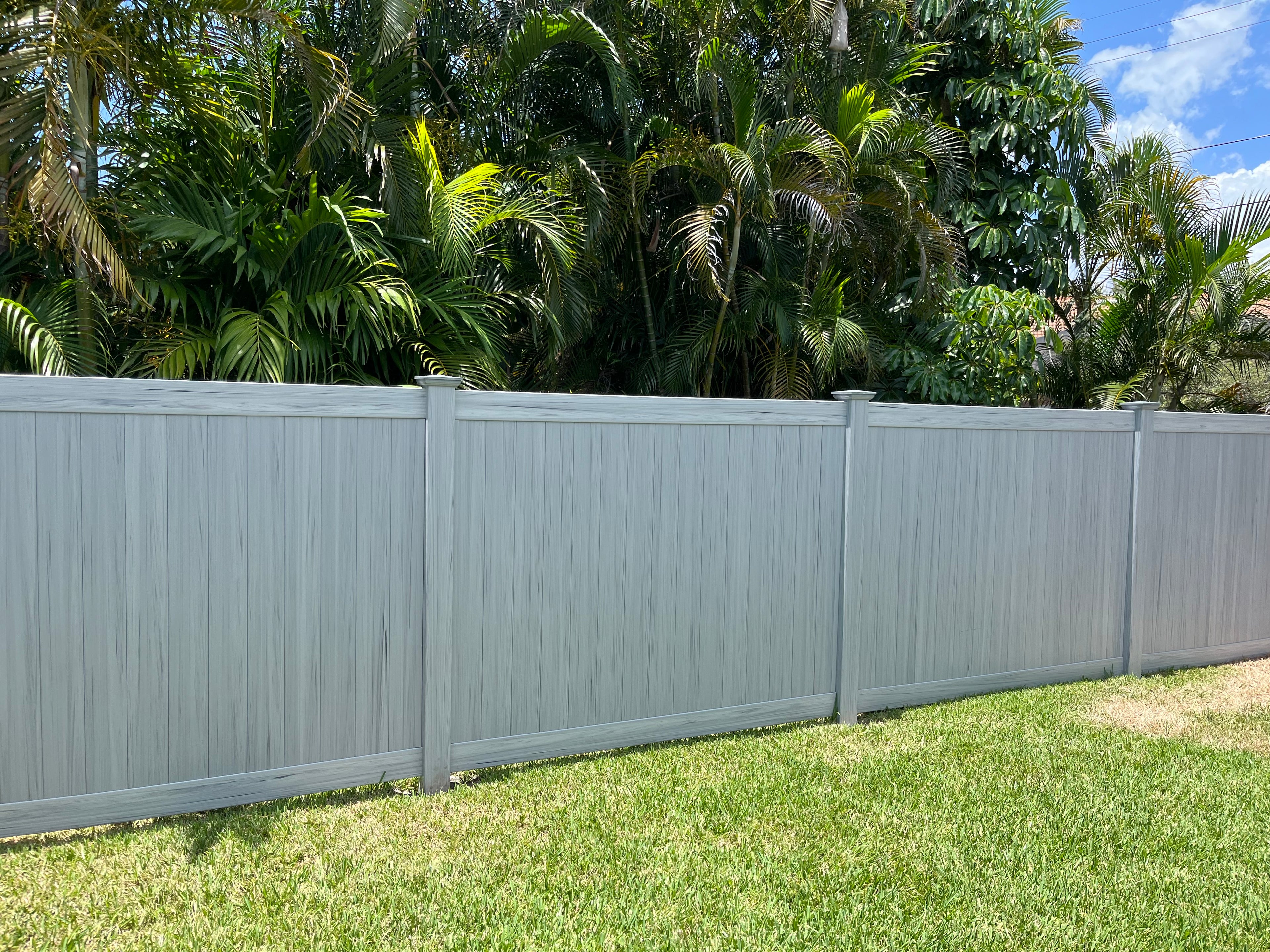 Weatherables Coastal Grey woodgrain vinyl privacy fence with greenery in the background