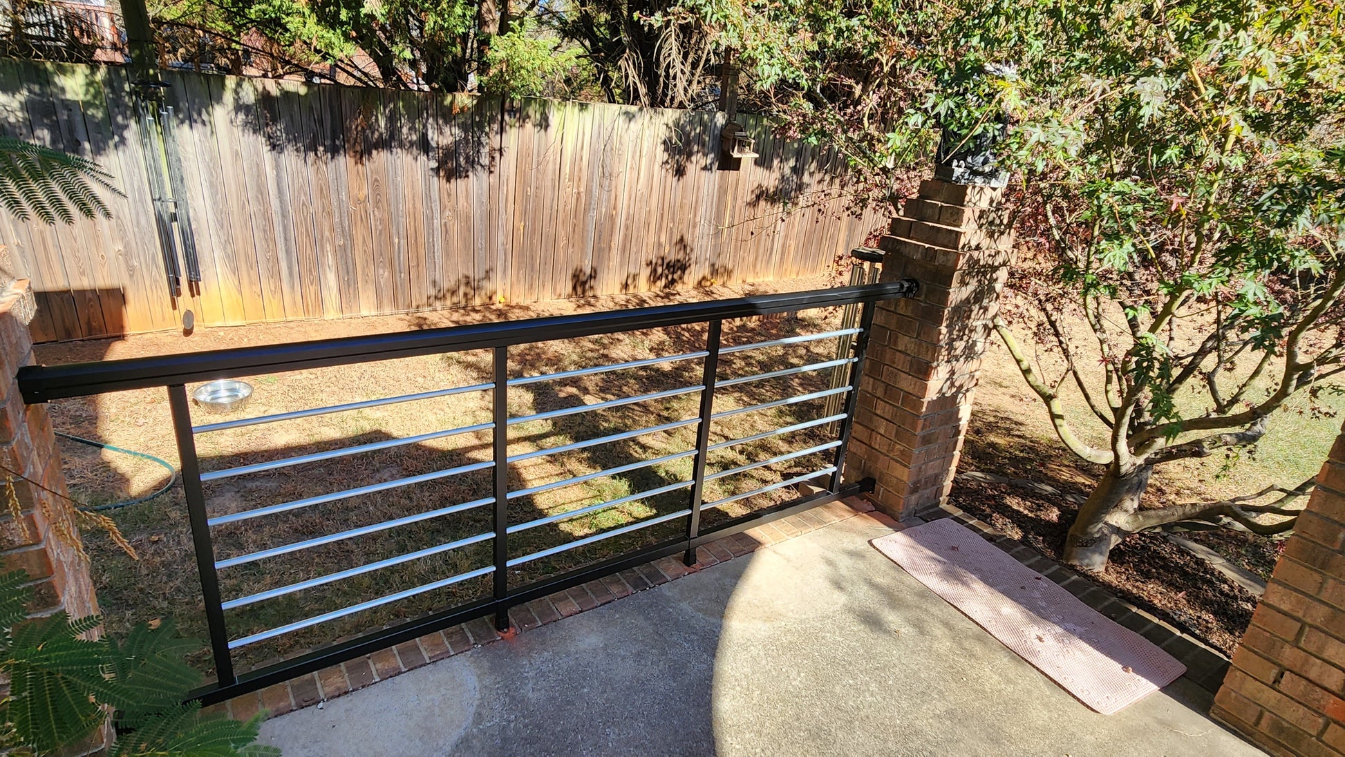 Weatherables Cornell black and silver aluminum rod railing on a patio with trees and wooden fence in the background