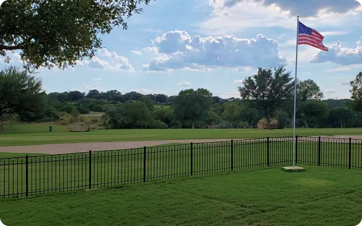 Golf course with a flagpole and American flag against a blue sky with clouds.