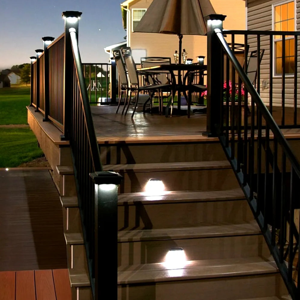 Outdoor deck with solar lights on steps and railing, table with chairs in background.
