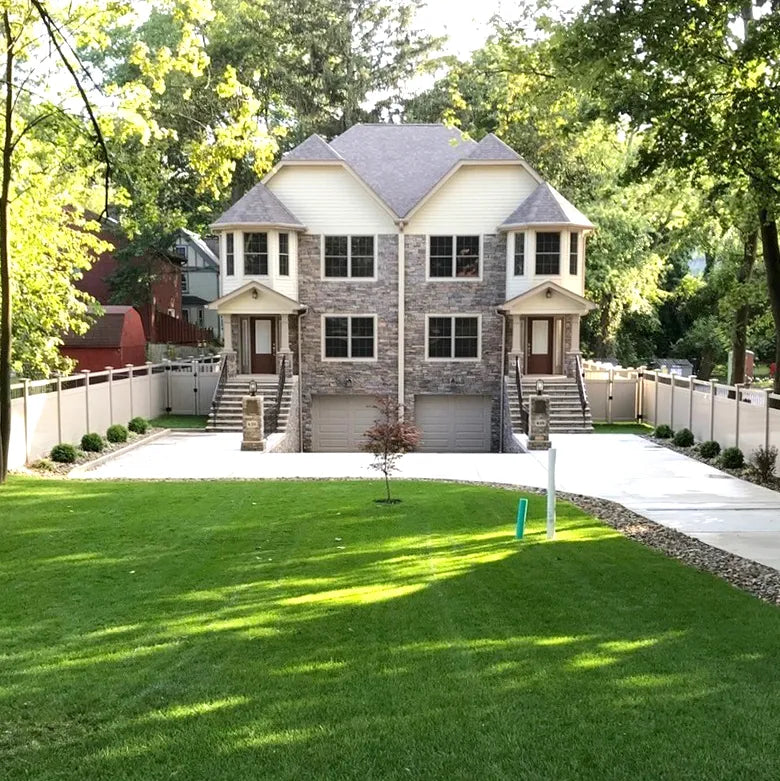 Two-story house with stone facade and gray roof, surrounded by greenery