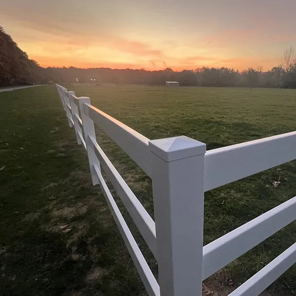 White fence running through a grassy field with a sunset sky.