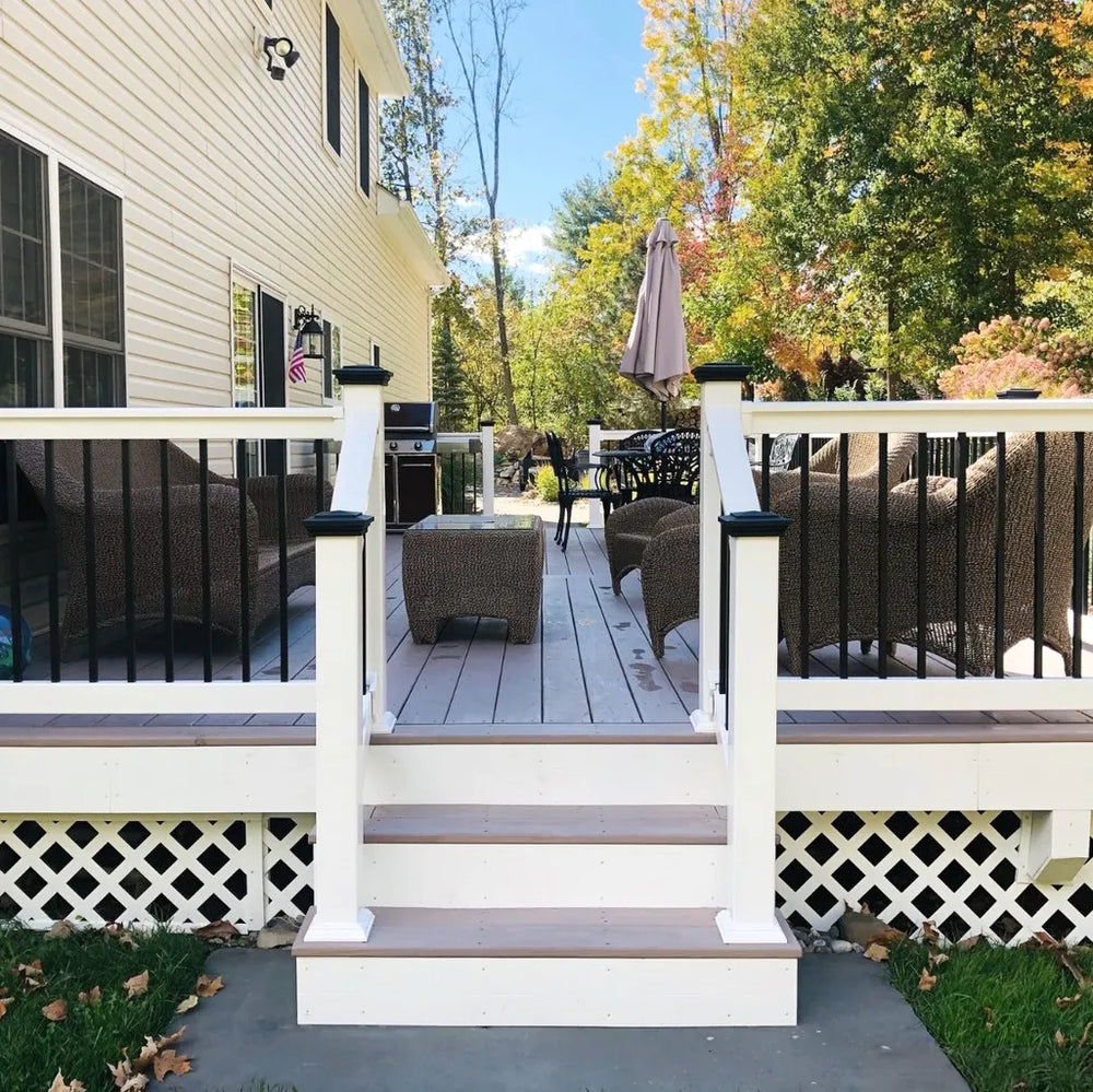 Backyard deck with outdoor furniture and a grill, surrounded by trees with autumn foliage.