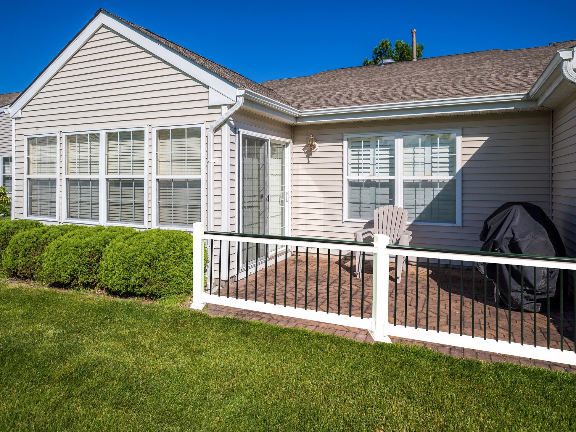 Backyard with Weatherables Jefferson white vinyl deckboard railing on a patio, lawn chairs, and a barbecue grill on a sunny day.