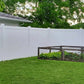 Backyard with a white fence, grass, and a wooden bench.