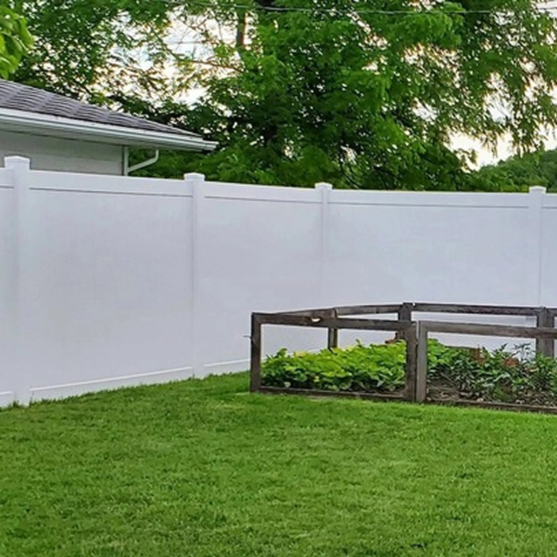 Backyard with a white fence, grass, and a wooden bench.