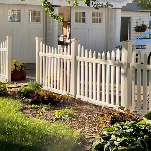 White picket fence in front of a house with a garden and car visible