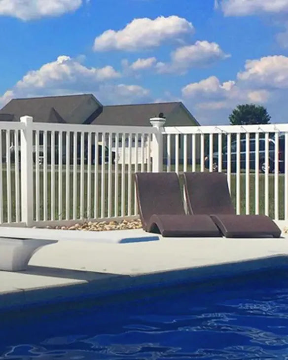 Two lounge chairs by a pool with a white fence and house in the background