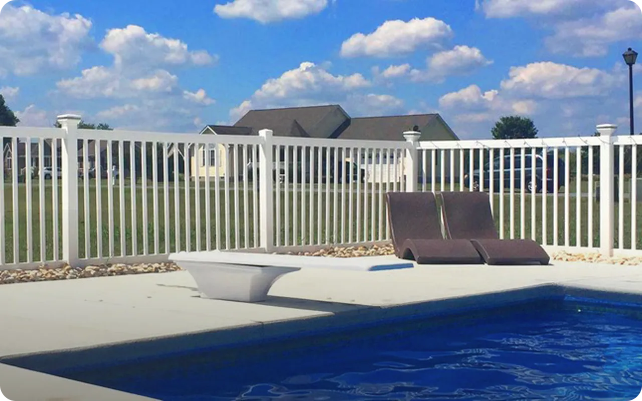 Pool area with lounge chairs, table, and white fence under a blue sky.