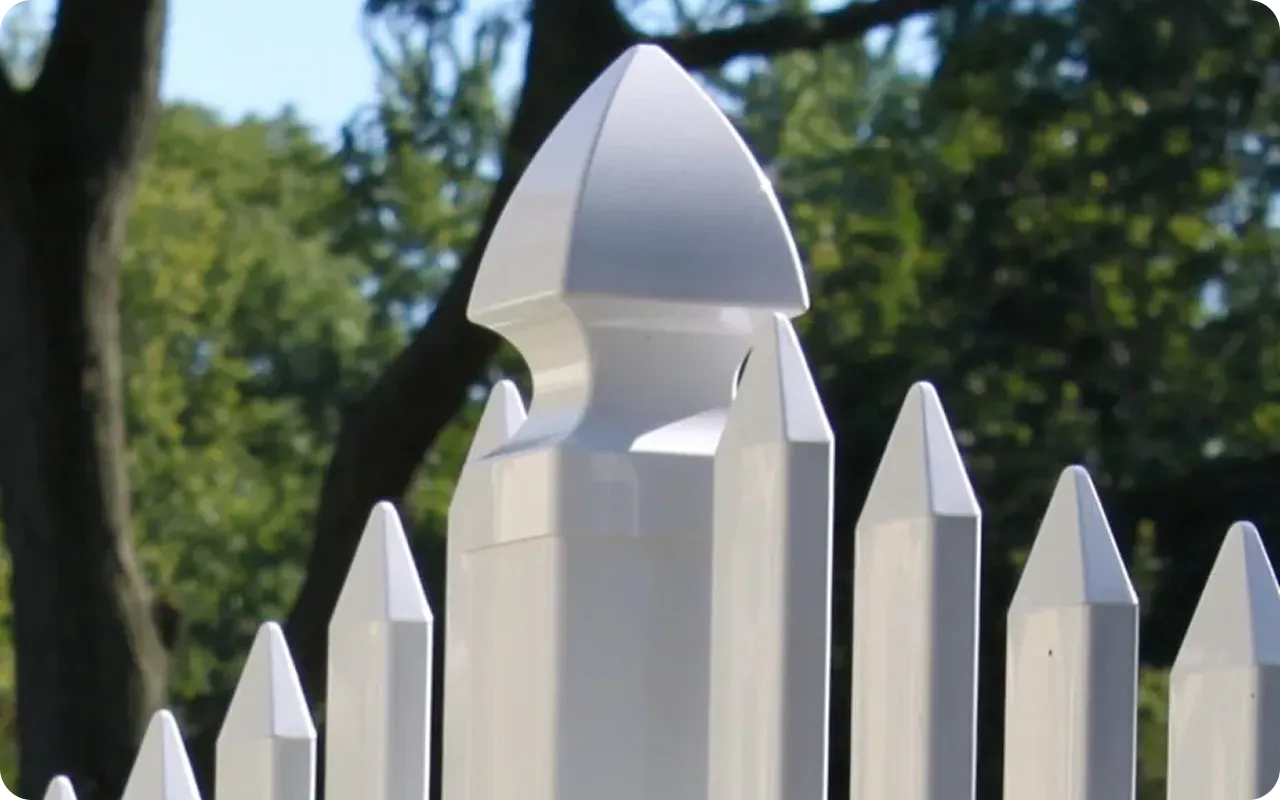 White picket fence with pointed top design against a blurred green background