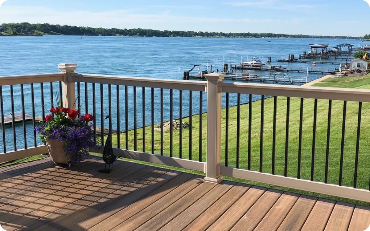 Wooden deck with railing overlooking a lake with boats and green grass.
