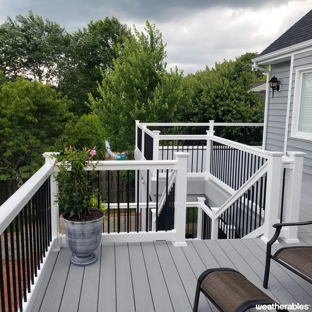 Deck with white railing, potted plant, and outdoor furniture with a view of trees and house.