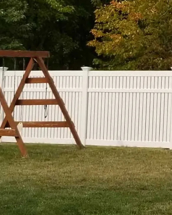 Wooden swingset,  a white fence with trees in the background
