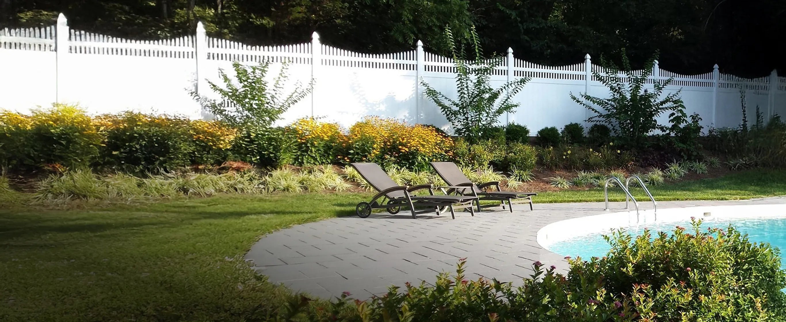 Pool area with lounge chairs, white fence, and greenery