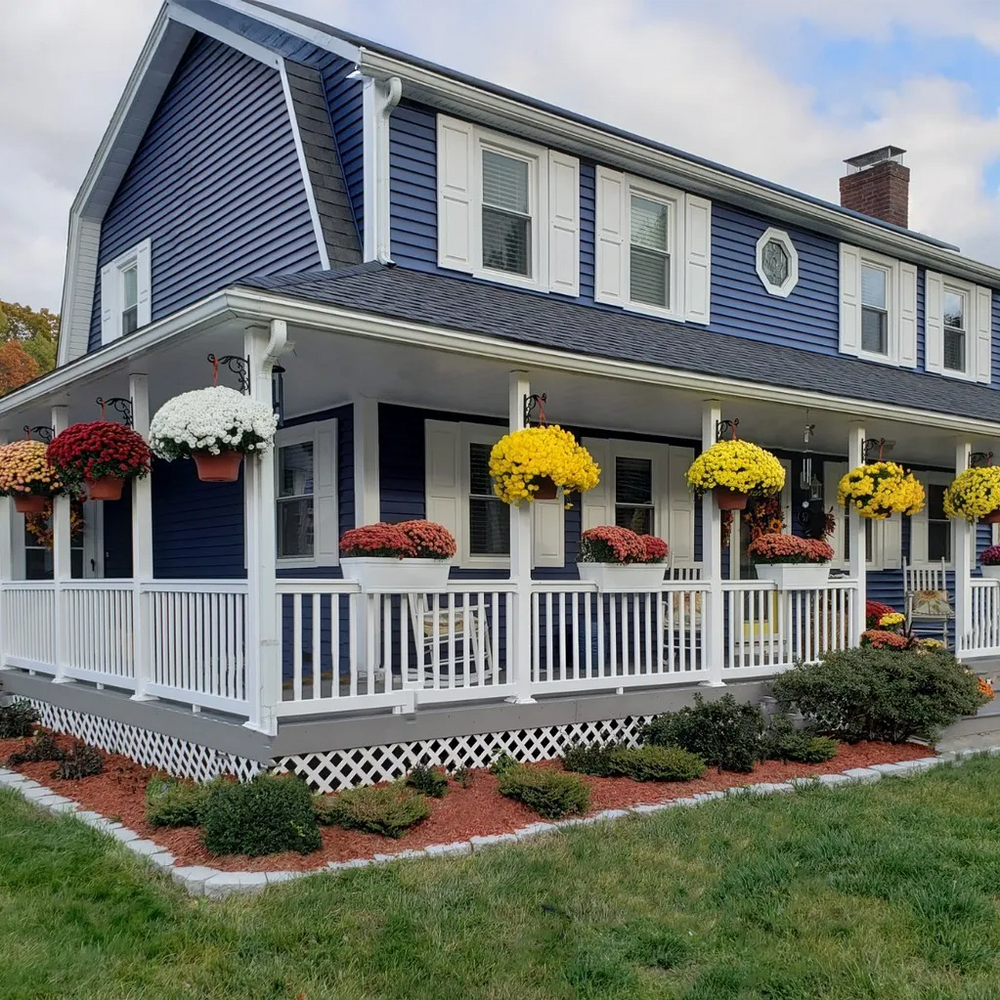 Two-story house with blue siding and white trim, featuring a porch with floral arrangements.