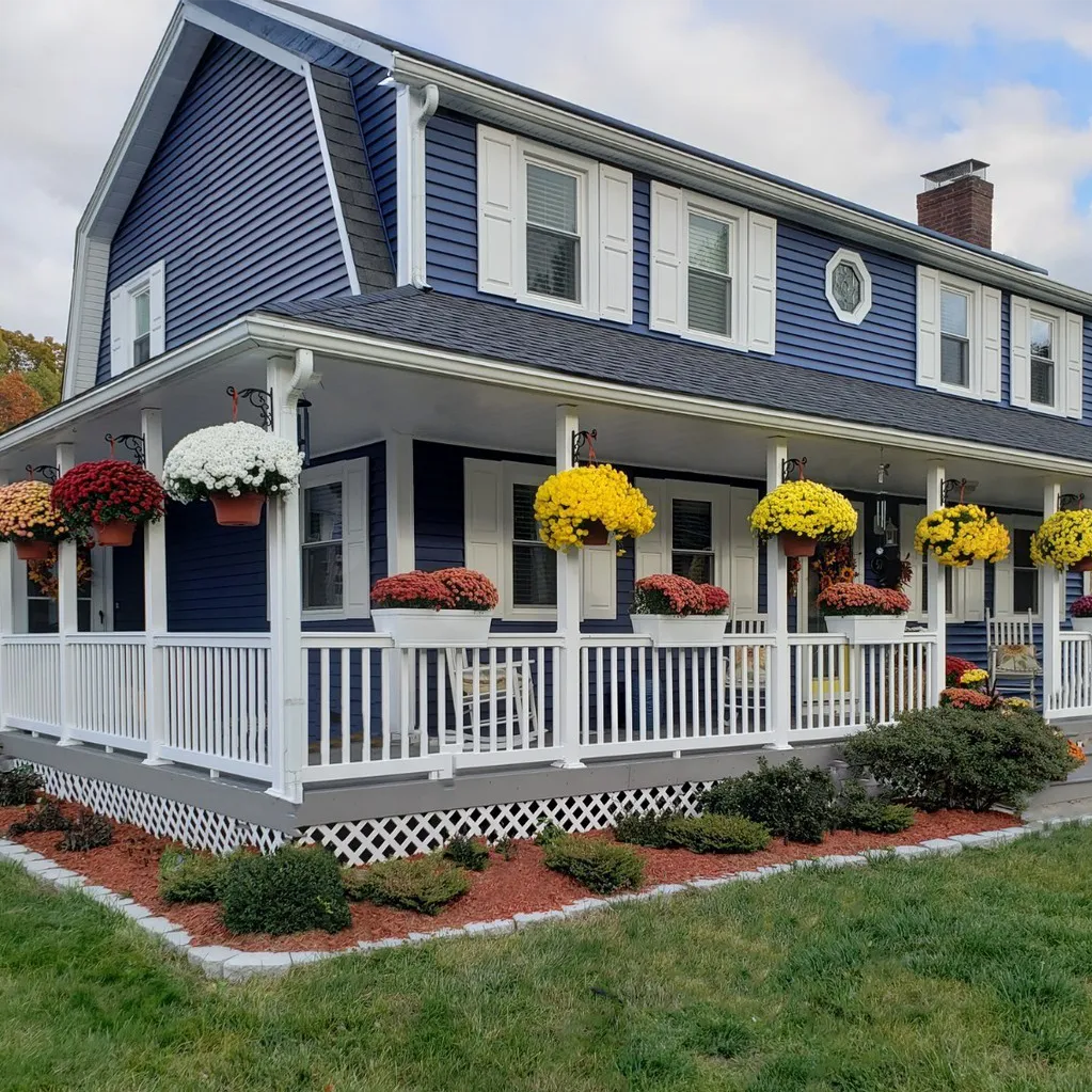 Two-story house with blue siding and white trim, featuring a porch with floral arrangements.